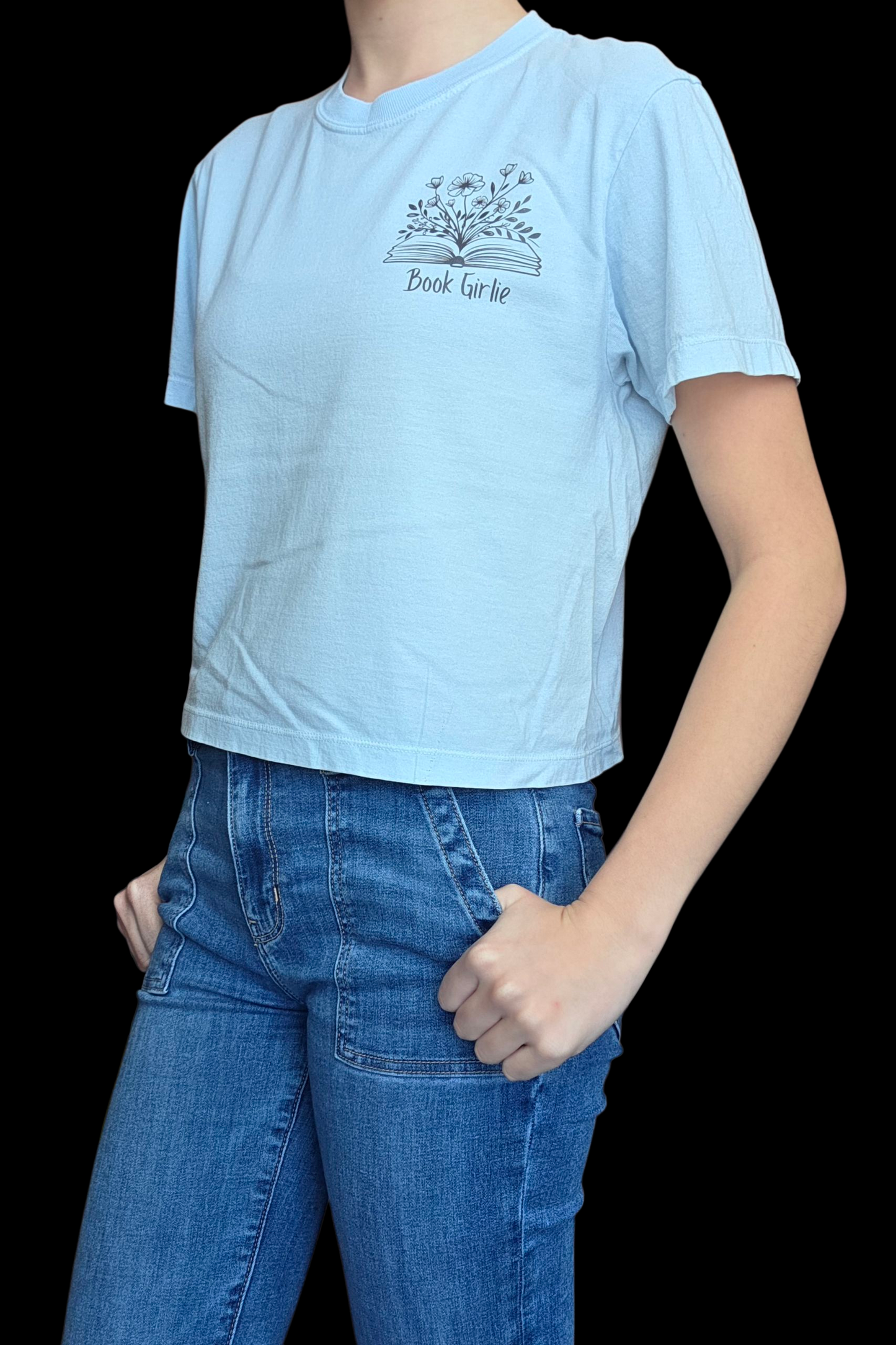 Person wearing a light blue t-shirt with a graphic design and blue jeans on a black background
