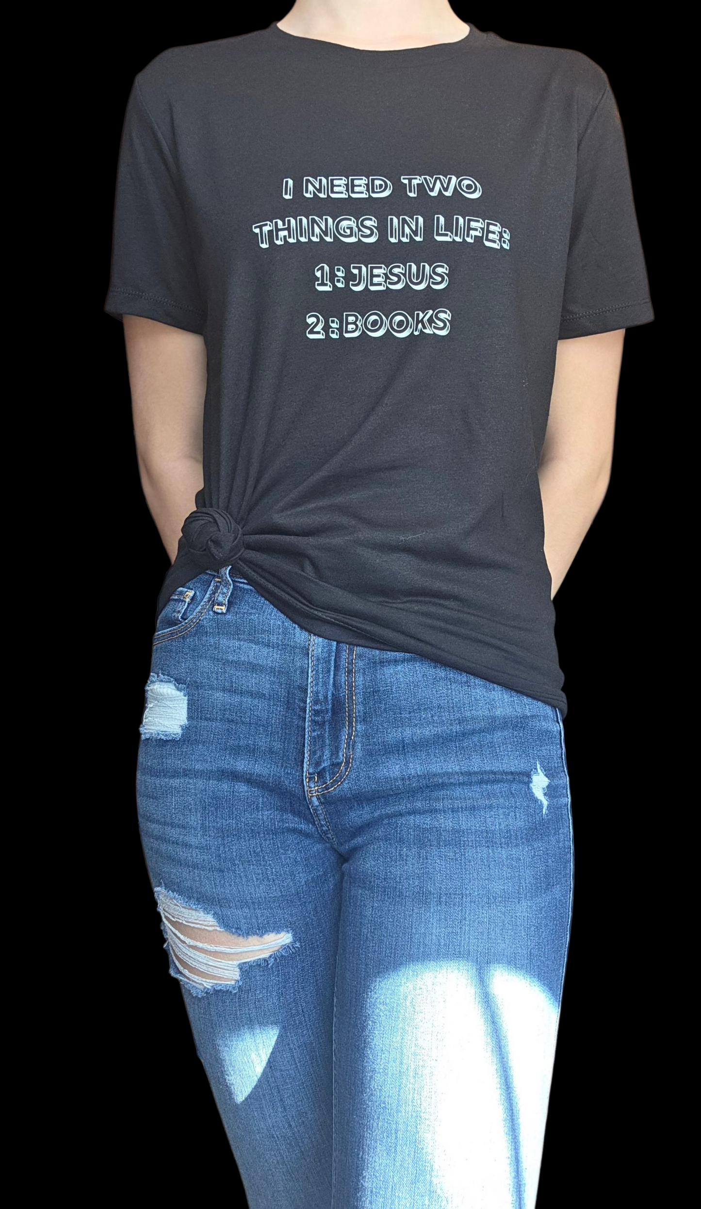 Person wearing a black t-shirt with text 'I NEED TWO THINGS IN LIFE: 1: JESUS 2: BOOKS' and blue jeans.
