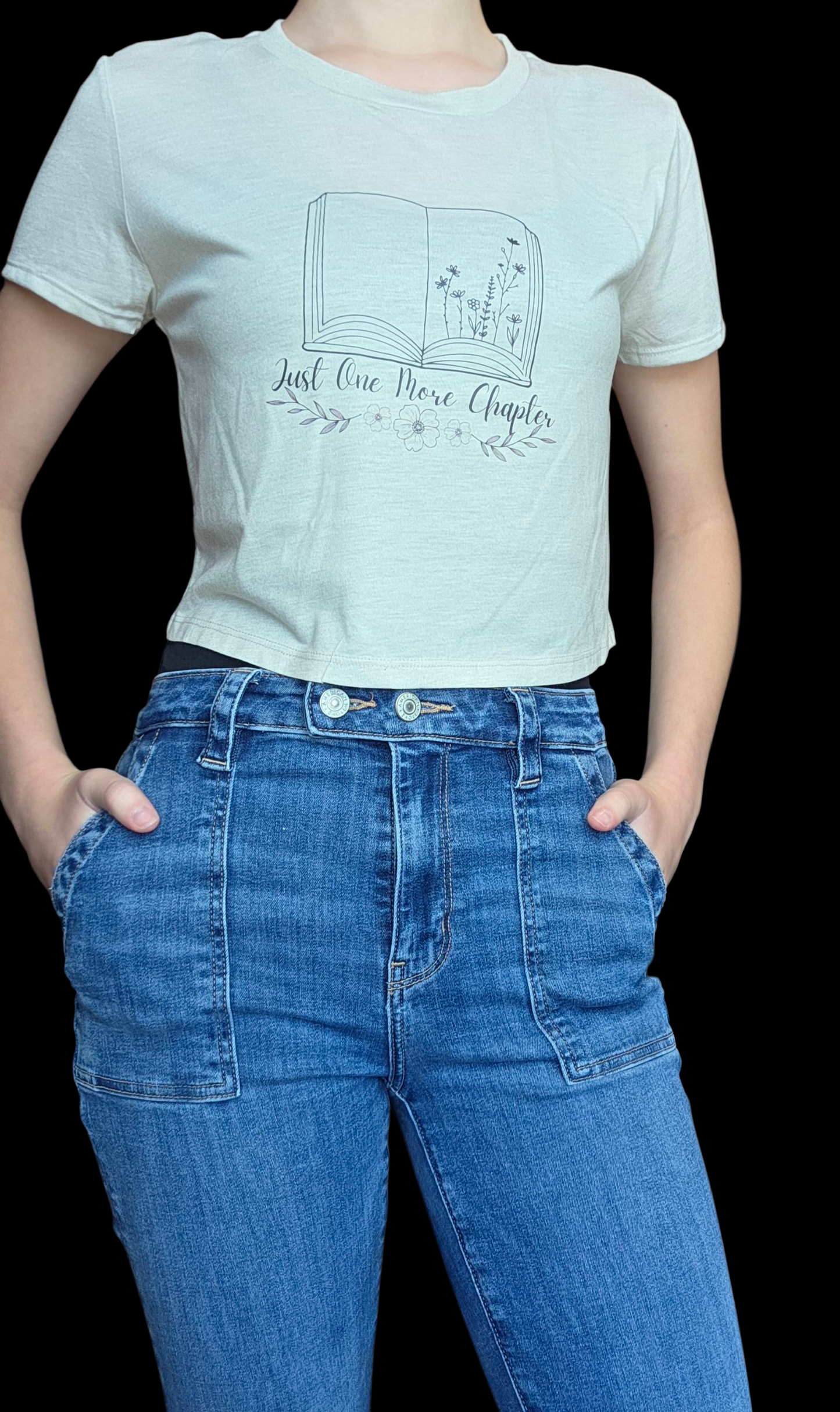 Person wearing a beige t-shirt with a graphic design and text, paired with blue jeans on a black background.